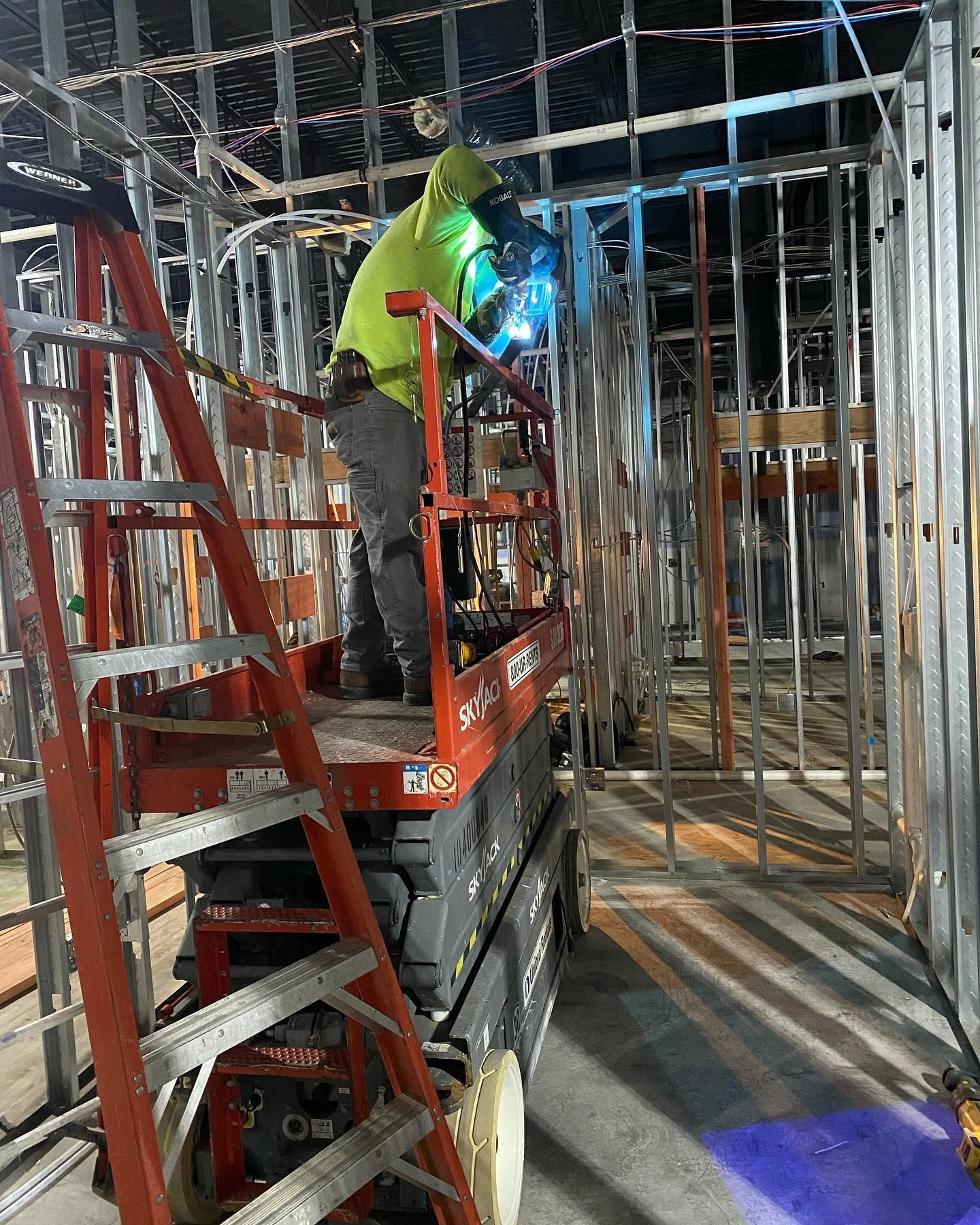 A man is welding on a scissor lift in a building under construction.