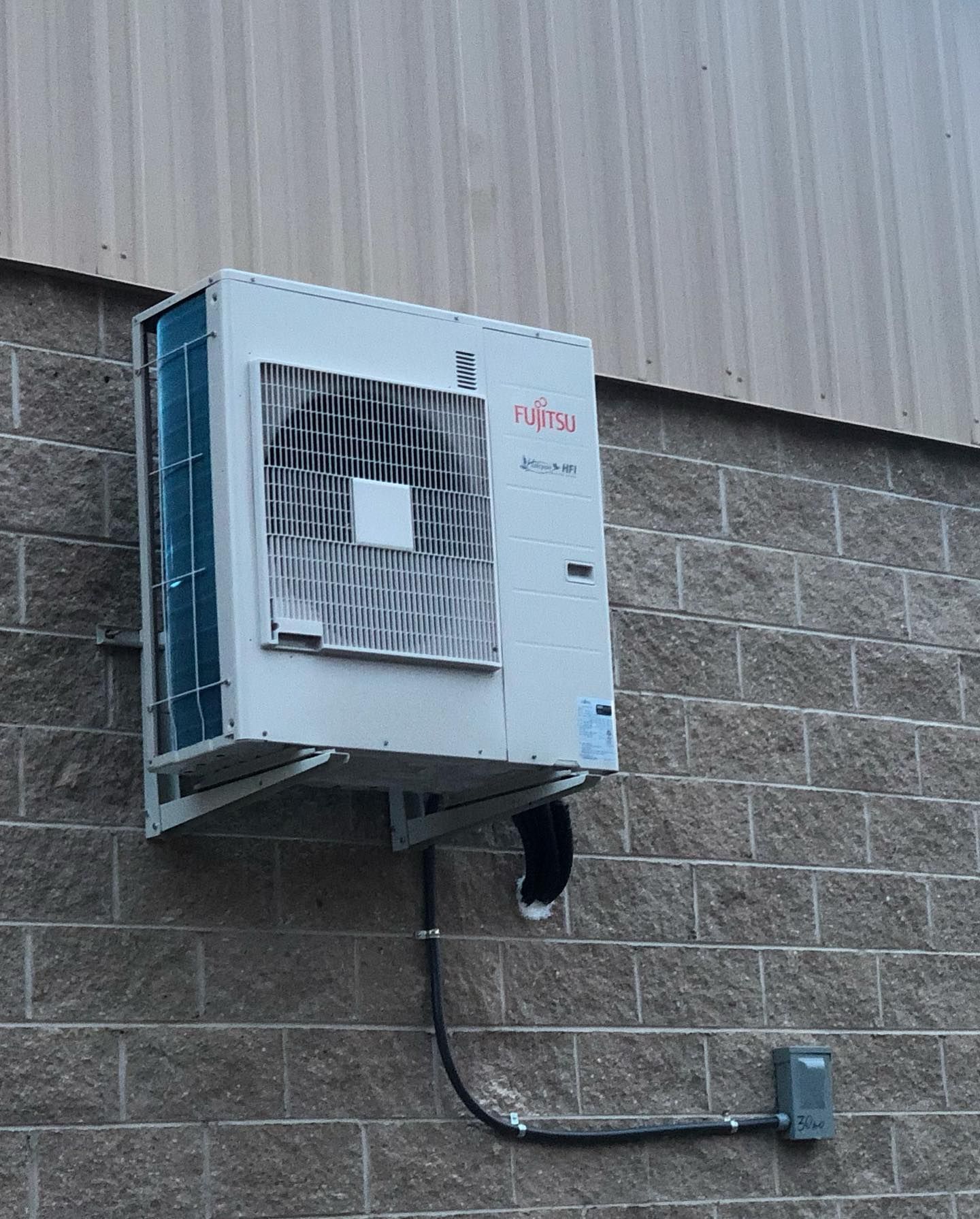 An air conditioner is mounted on the side of a brick building.