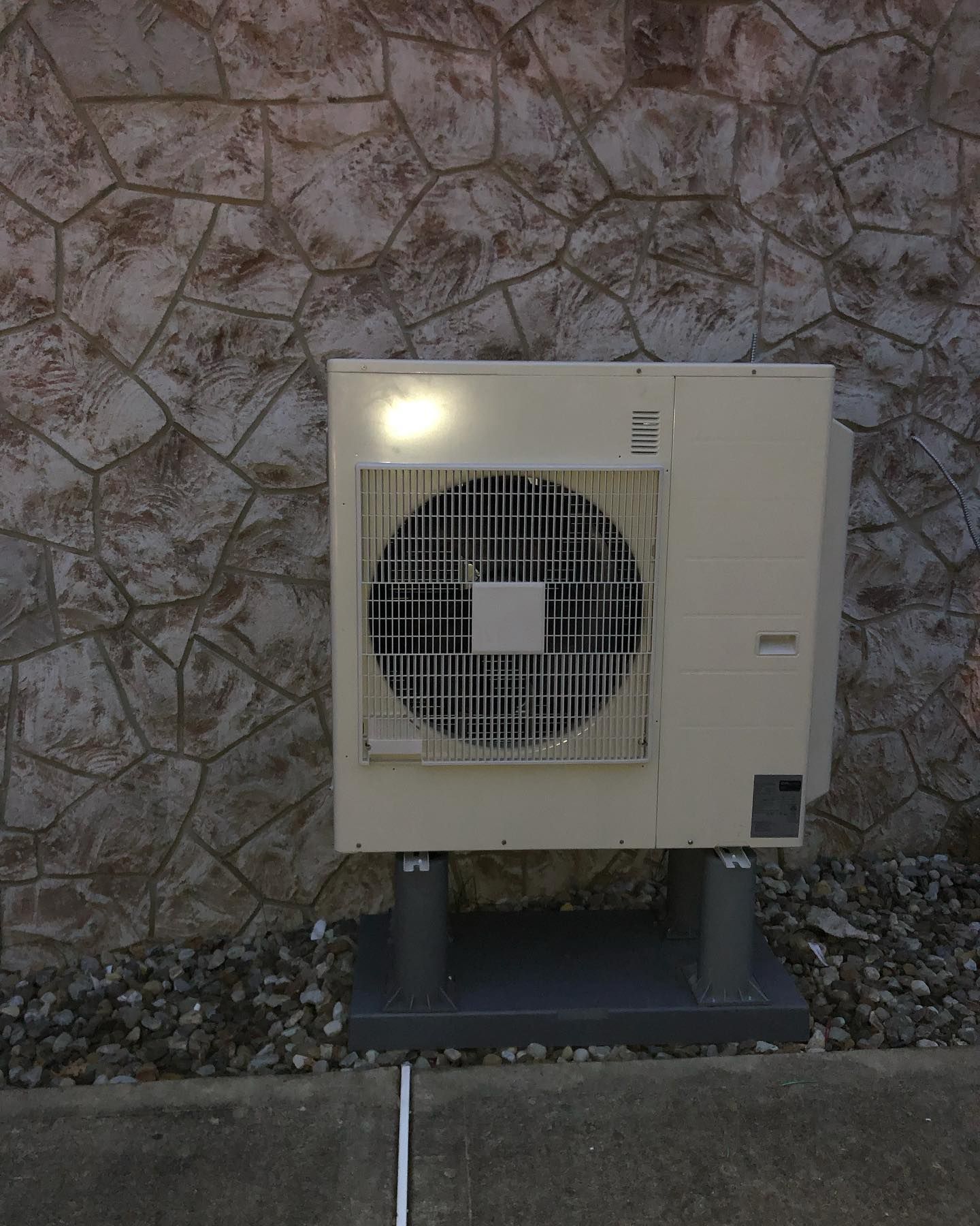 A white air conditioner is sitting in front of a stone wall