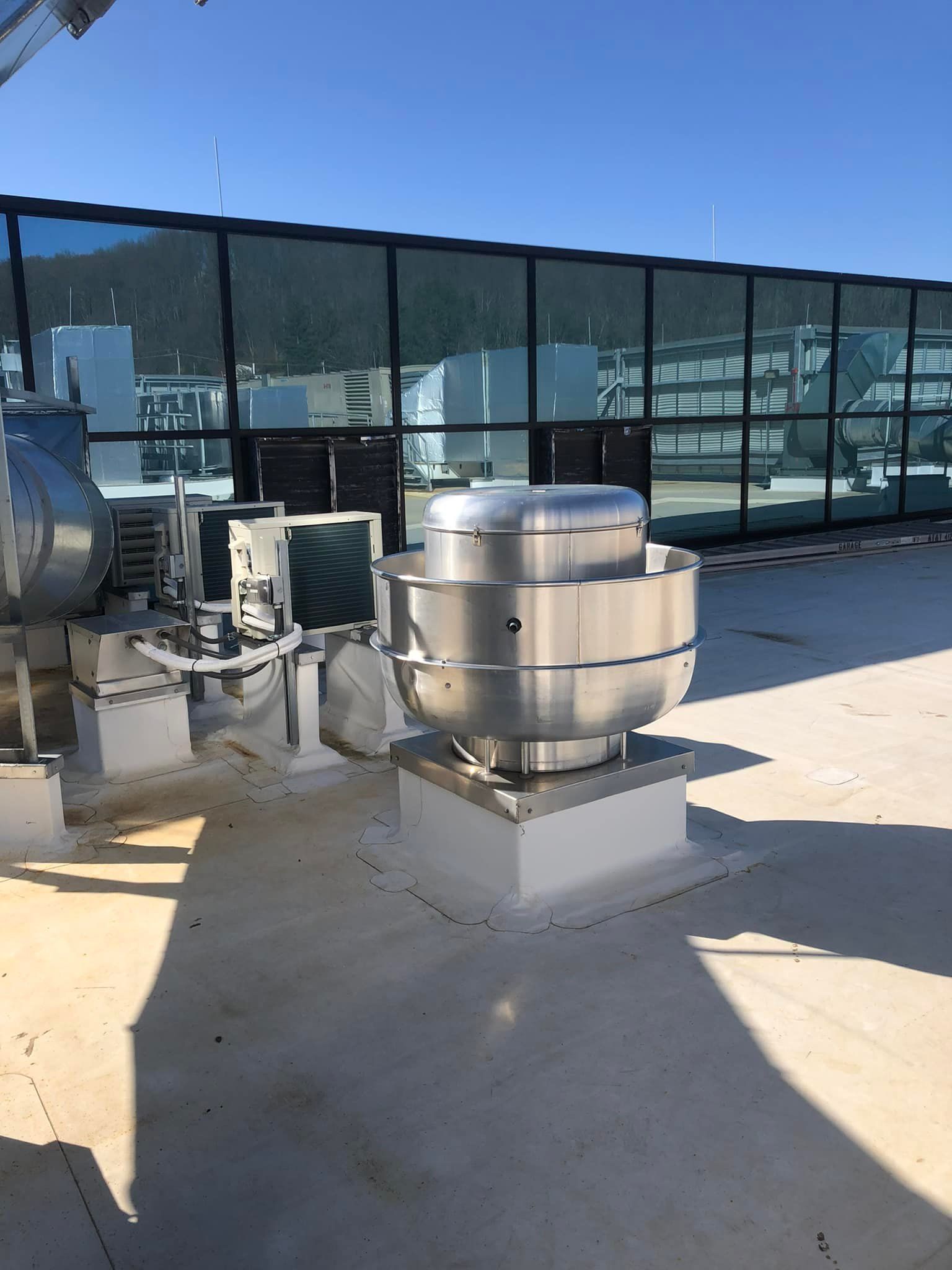 A large stainless steel fan is sitting on top of a roof.