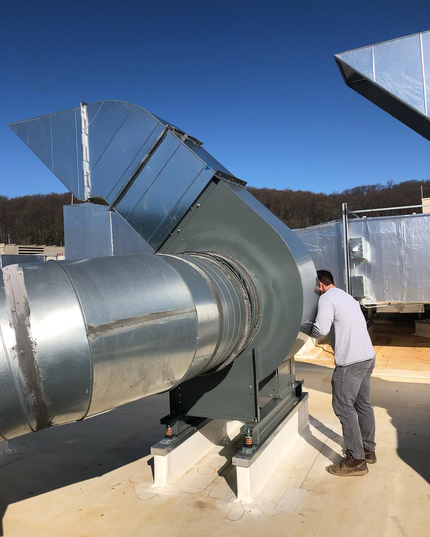 A man is working on a large fan on the roof of a building.