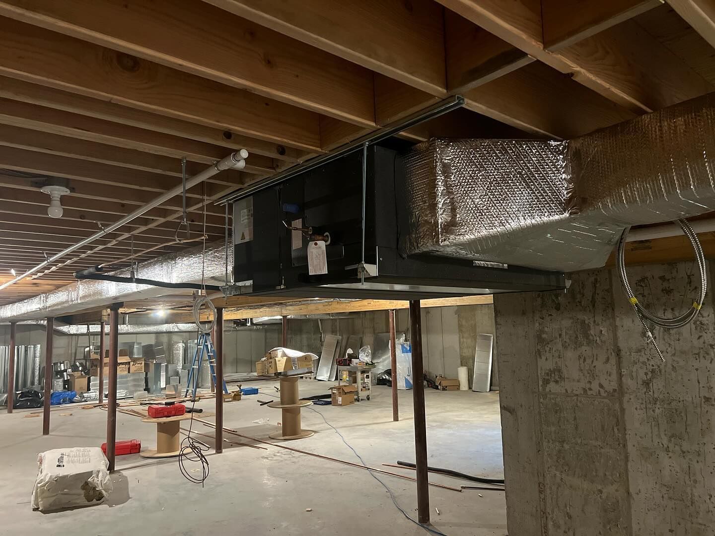 A basement under construction with a ventilation system hanging from the ceiling.