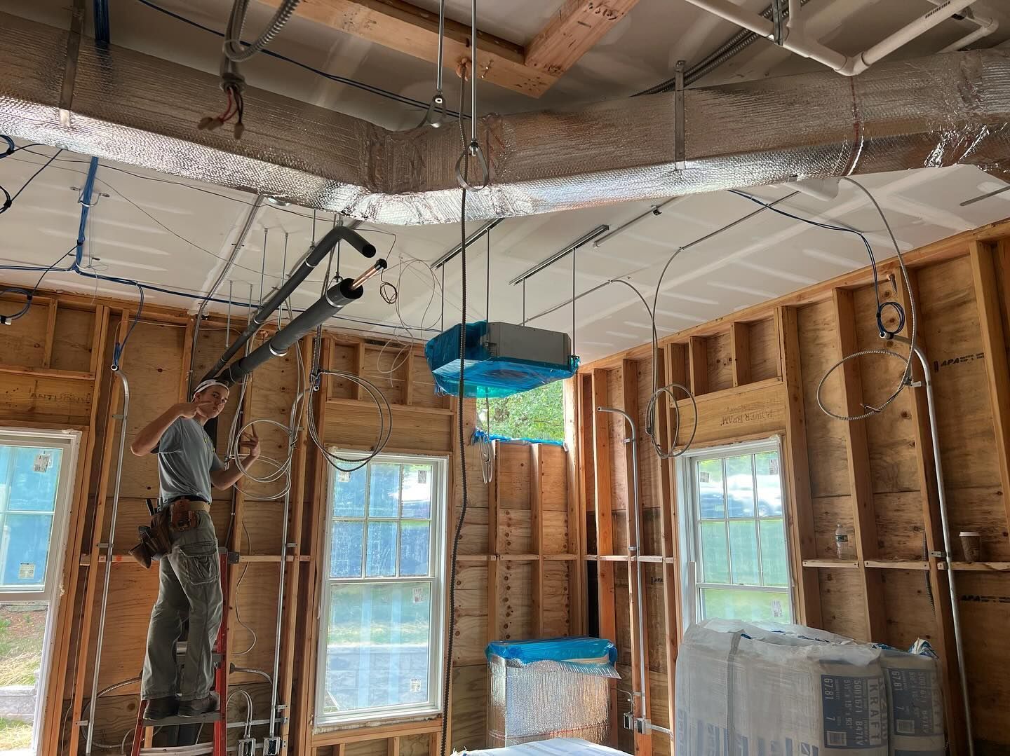 A man is standing on a ladder in a room under construction.