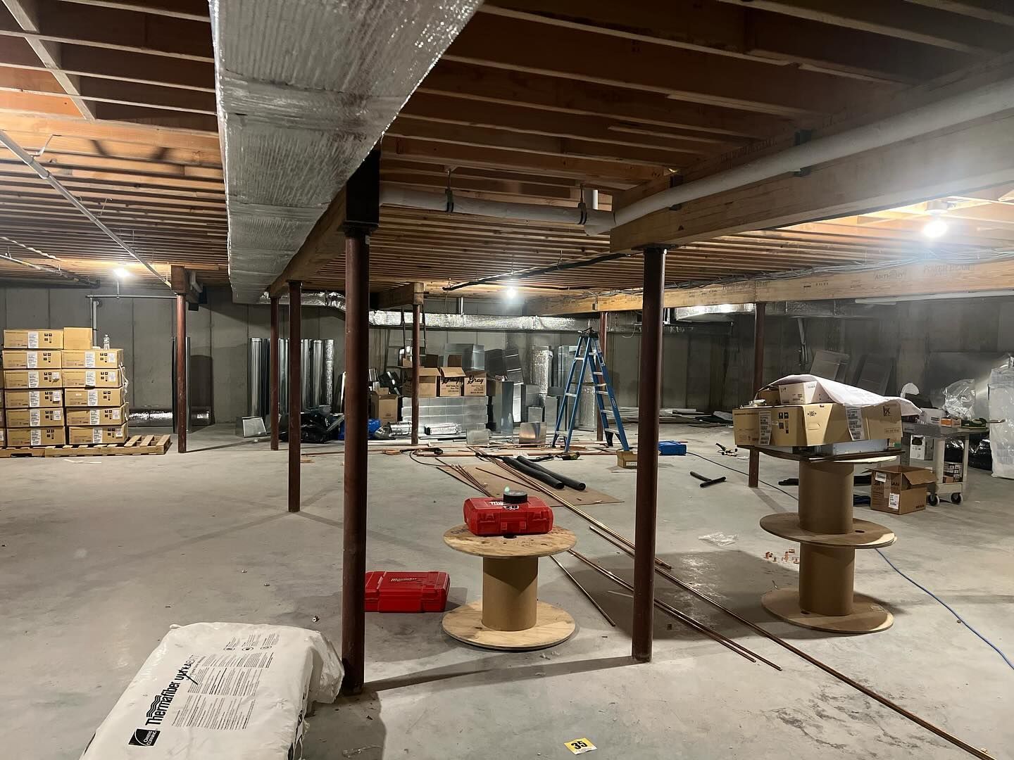 A basement under construction with wooden beams and spools of wire.