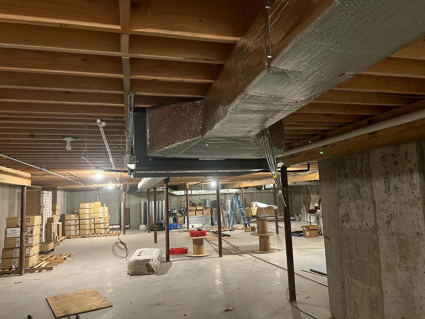 A basement under construction with a large duct hanging from the ceiling.