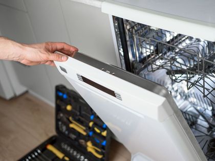 A person is fixing a dishwasher in a kitchen.