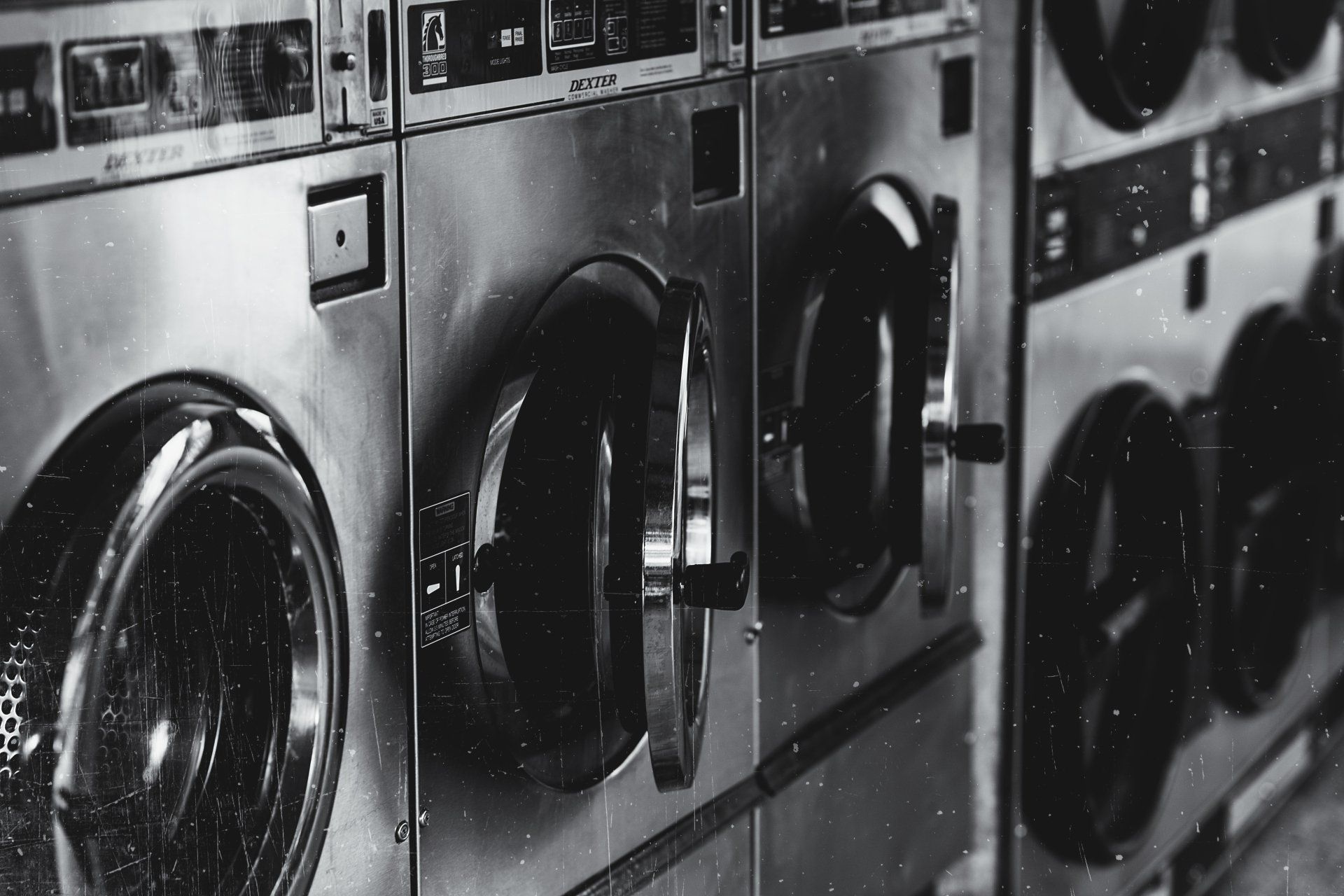 A black and white photo of a row of washing machines in a laundromat.