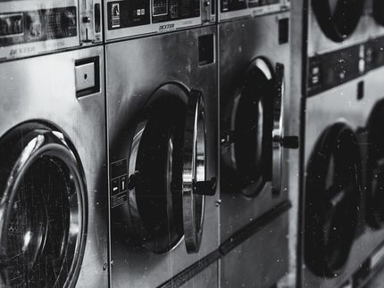 A black and white photo of a row of washing machines in a laundromat.