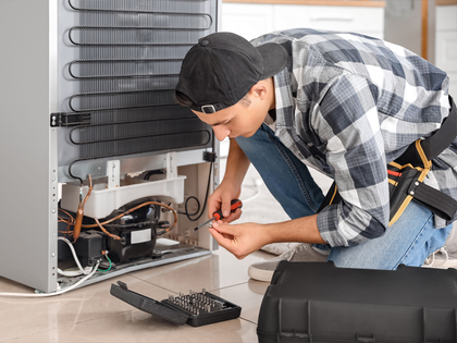 A man is fixing a refrigerator in a kitchen.