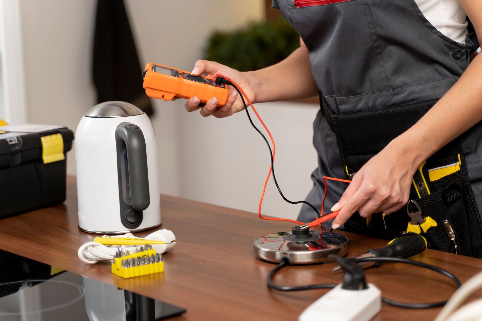 A woman is fixing an electric kettle with a multimeter.