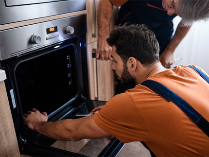 Two men are working on an oven in a kitchen.