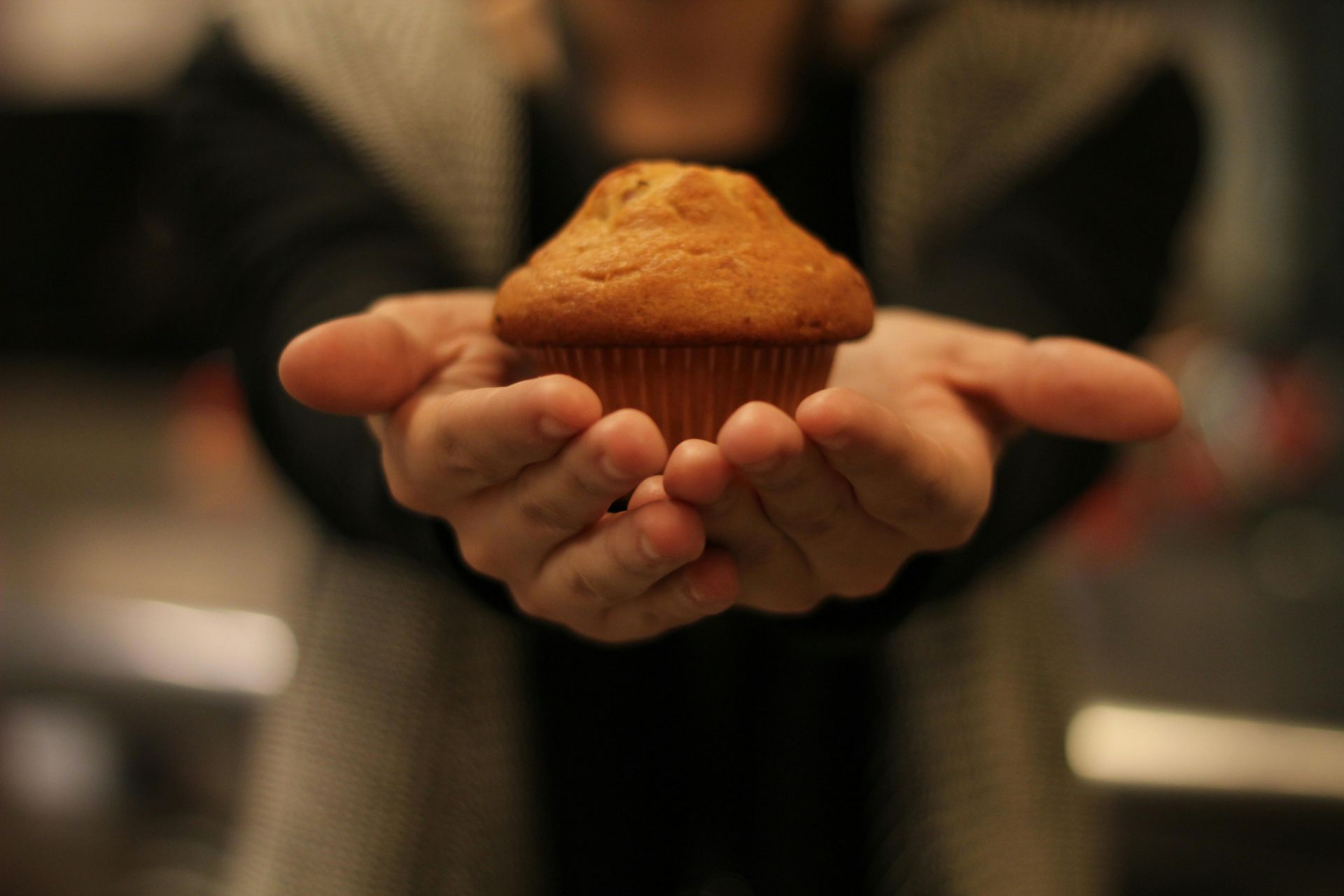 Person holding a golden muffin in cupped hands, offering it forward.