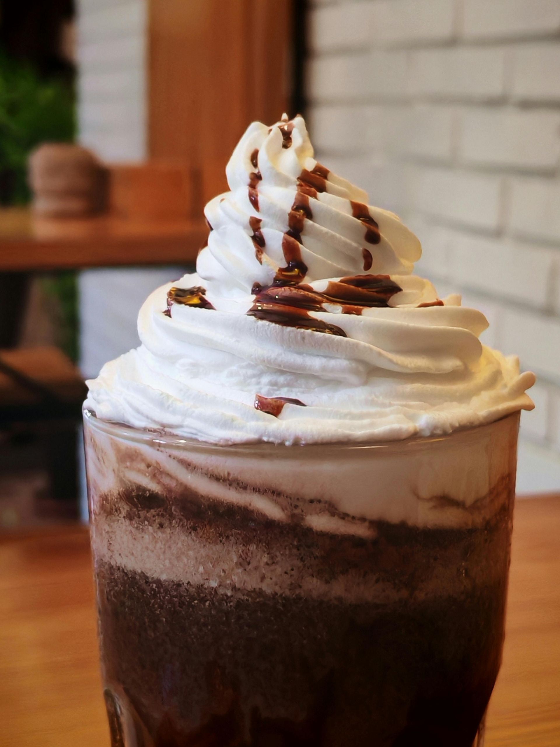 Chocolate drink topped with whipped cream and chocolate drizzle, in a glass on a wooden surface.