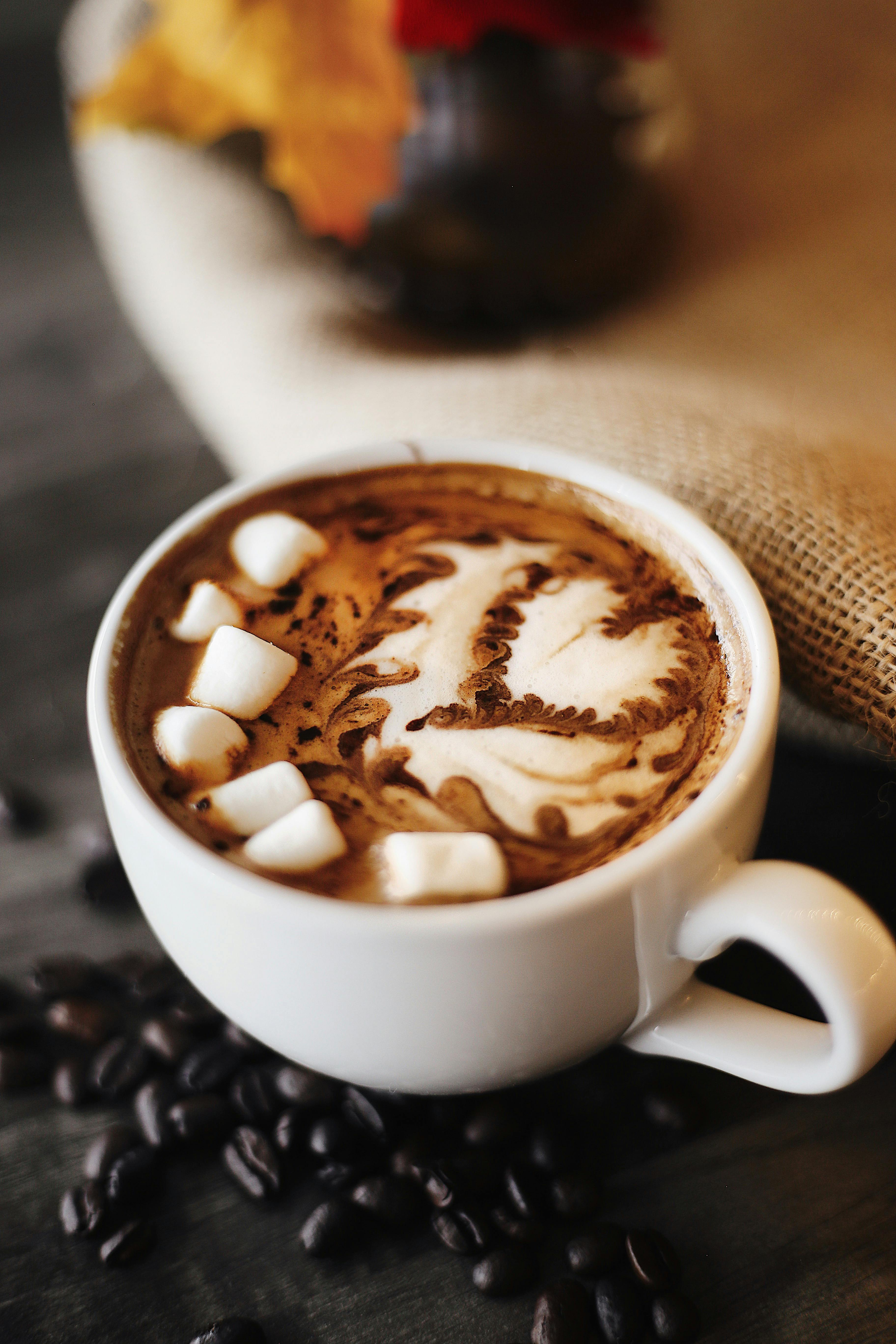 Cup of coffee with marshmallows and latte art on a table with coffee beans.