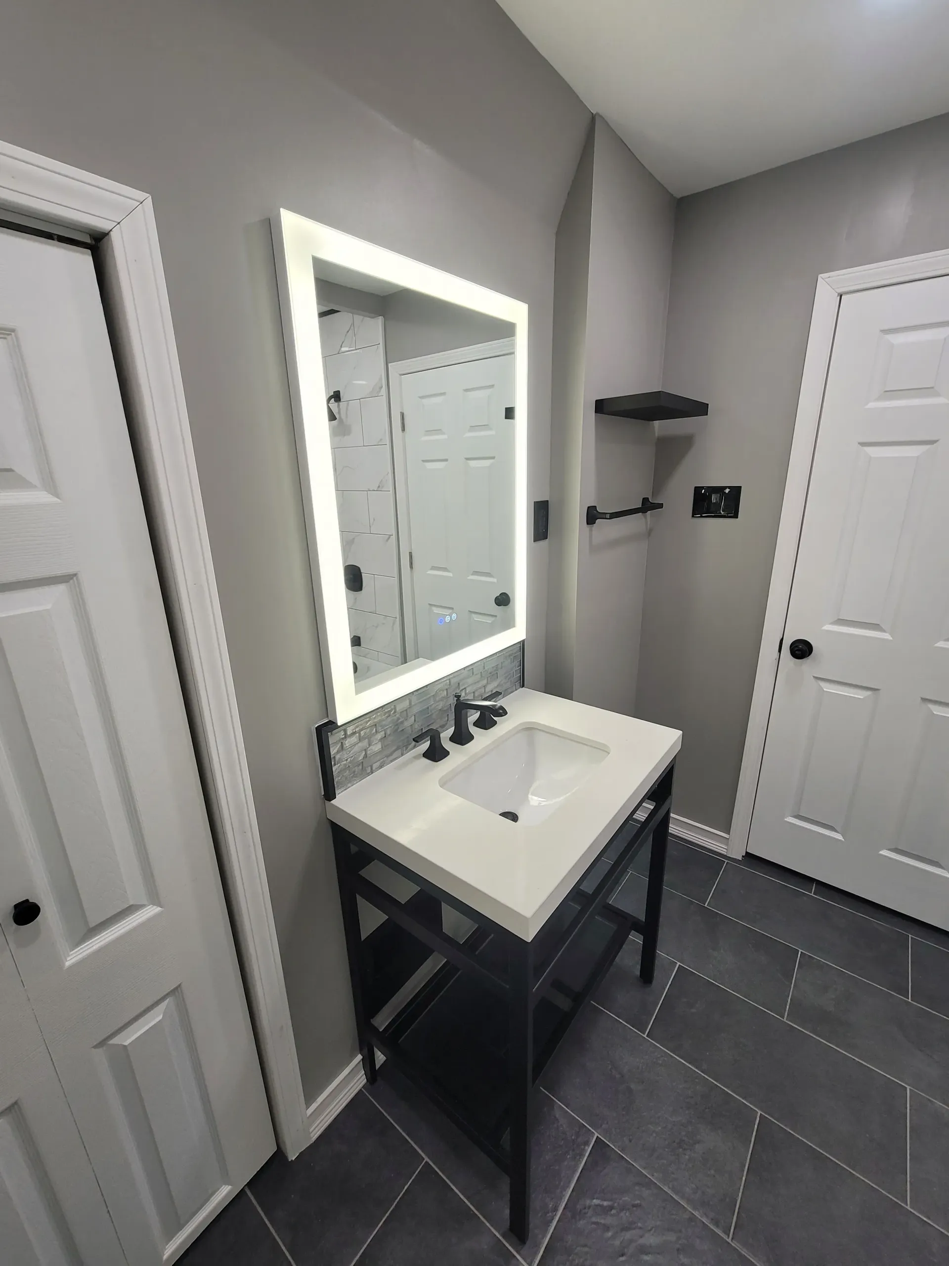 Modern bathroom with gray walls, a white countertop vanity with black fixtures, and a lit mirror