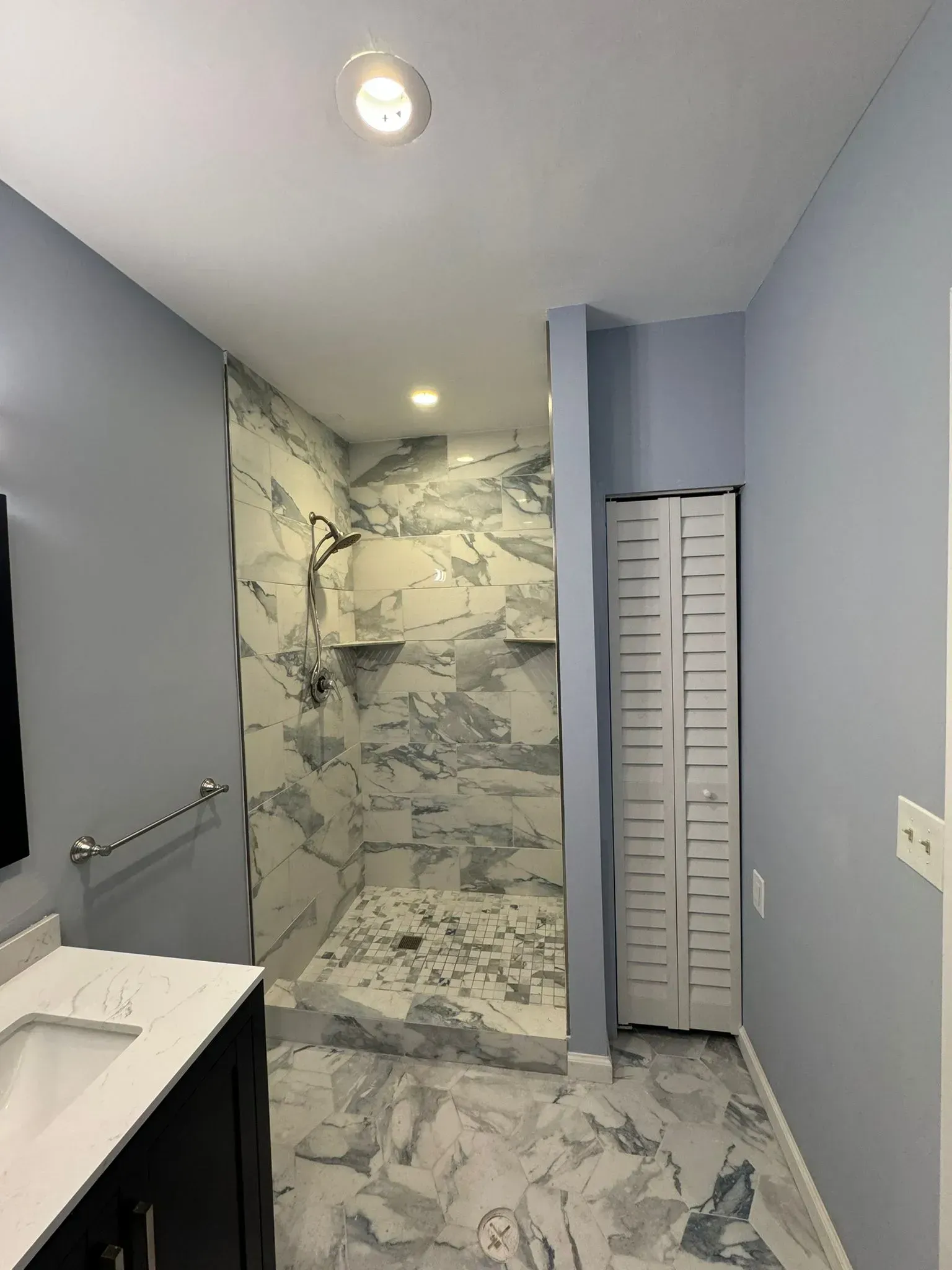 Bathroom with marble shower, gray floor tiles, and light blue walls. A white shuttered cabinet sits to the right.
