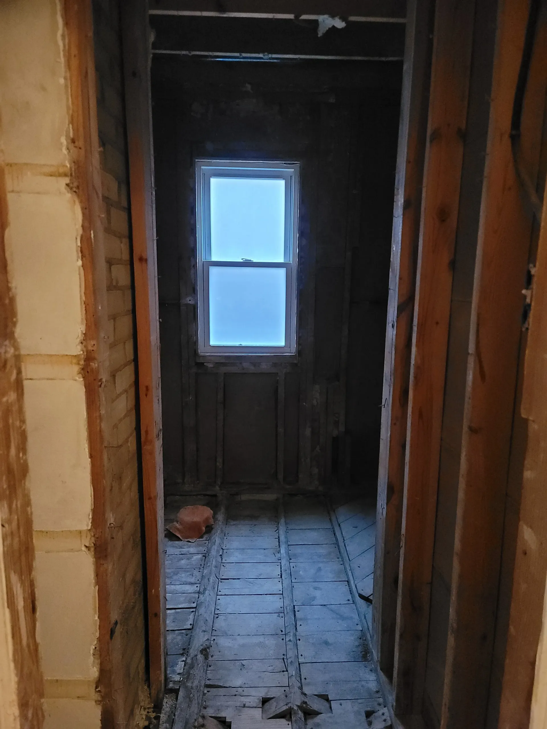 A narrow unfinished hallway with a window at the end
