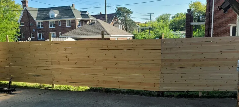 A long wooden fence with a neighborhood in the background on a sunny day