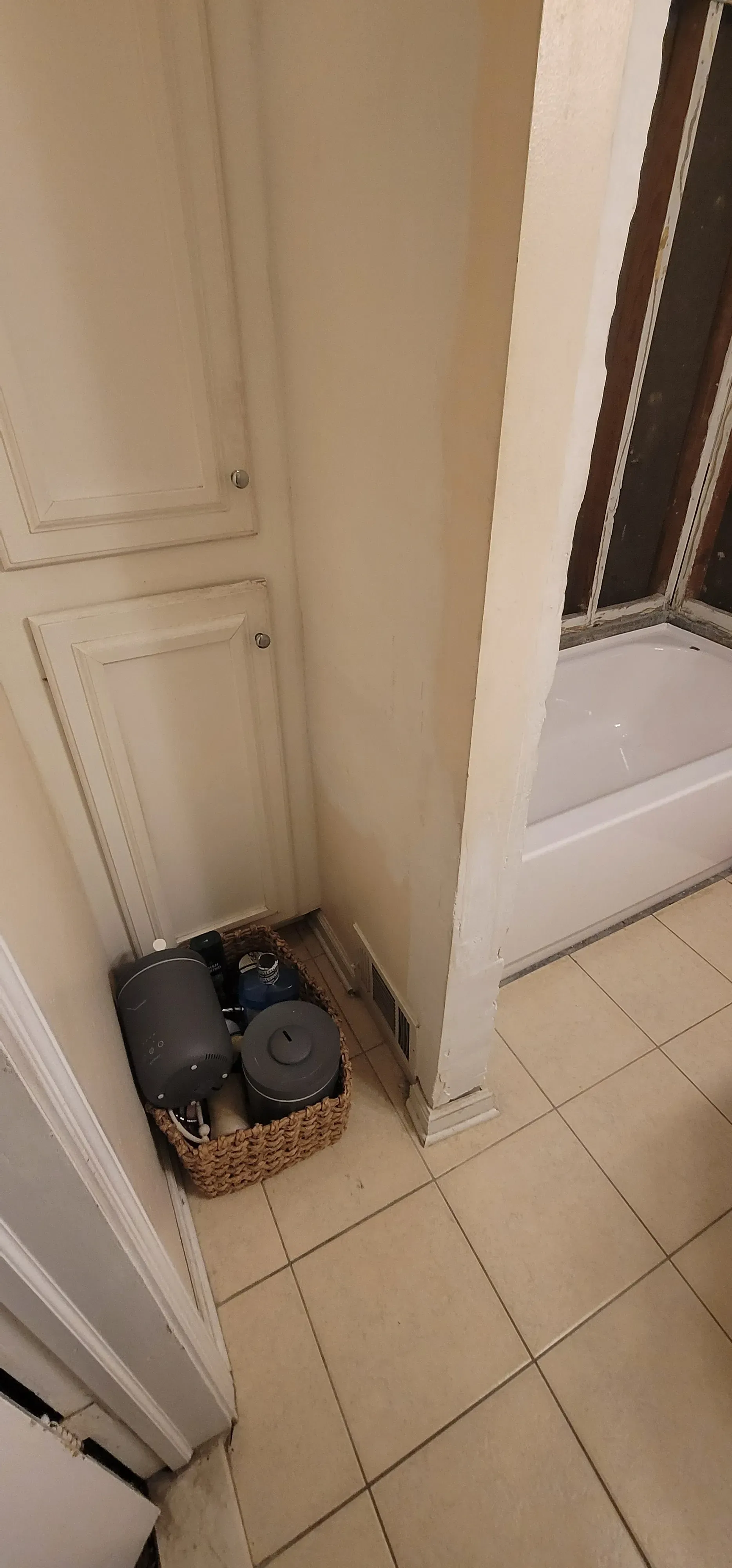 A small wicker basket with gray items sits in the corner of a tiled bathroom