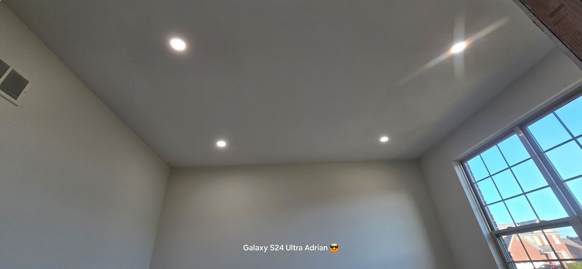 An interior shot of a room with recessed lights in the ceiling and a window with a view of the outdoors