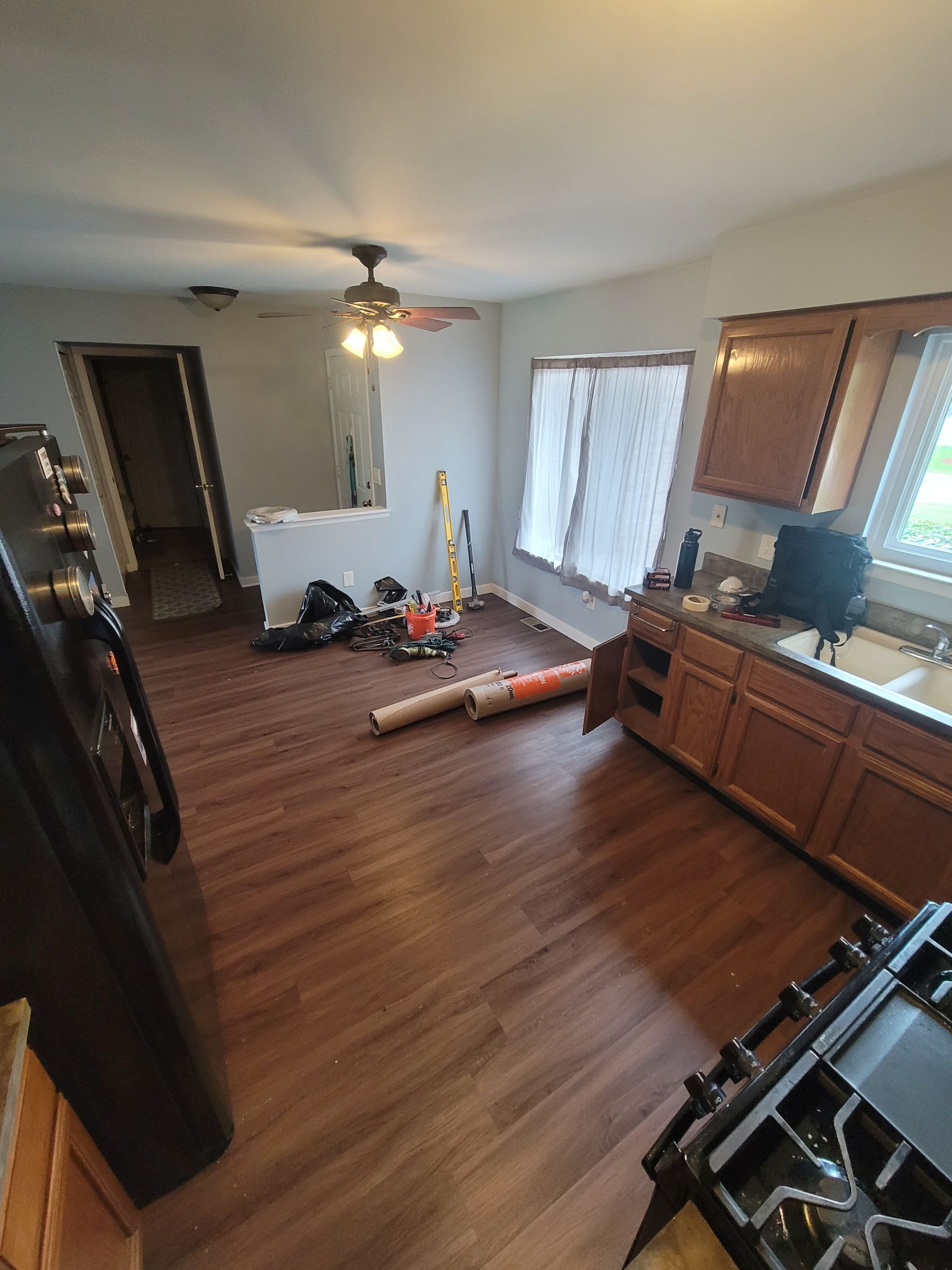 A kitchen with wooden cabinets , a stove , a refrigerator and a ceiling fan.