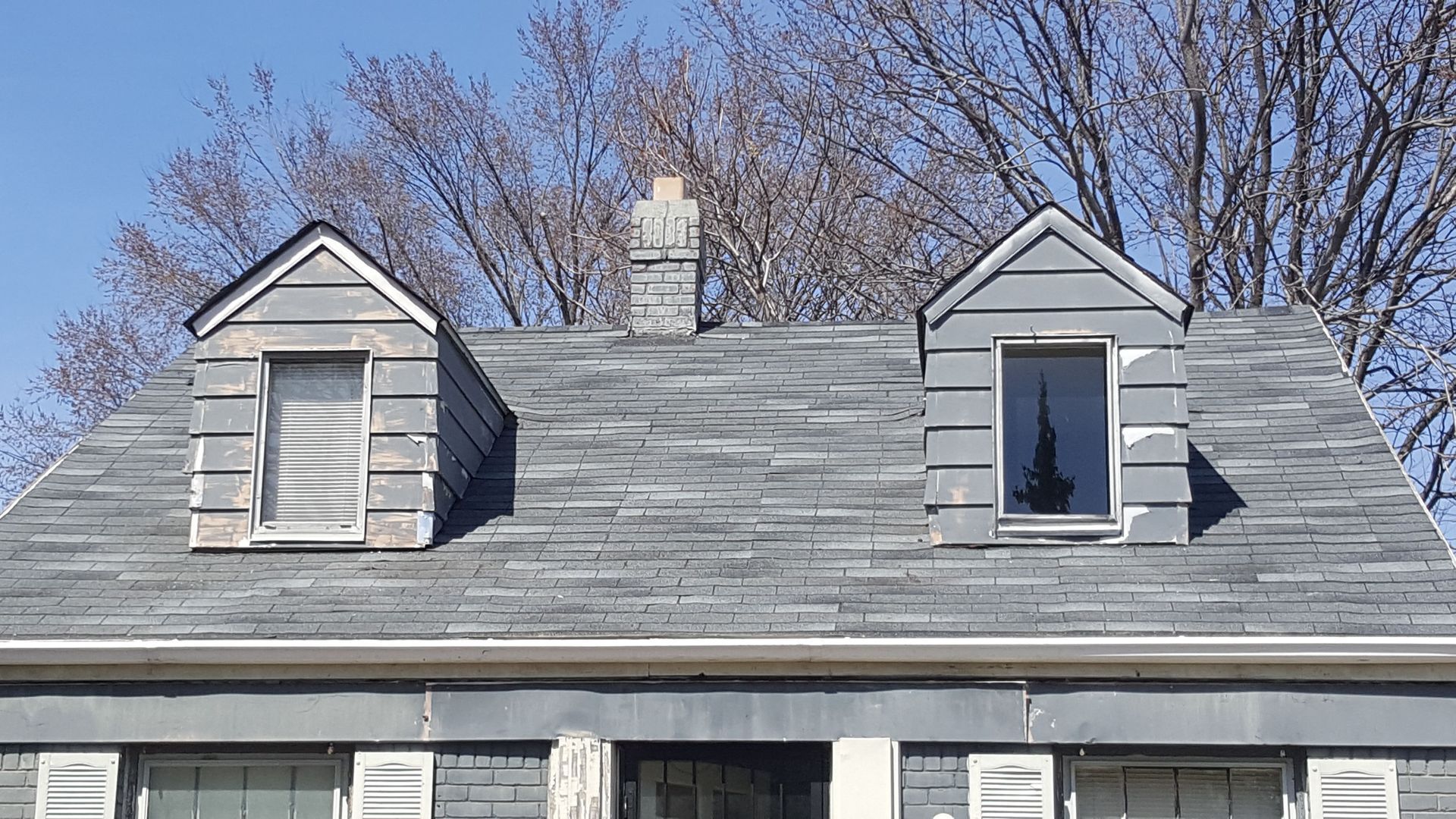 A gray house roof with two dormers and a central chimney against a blue sky