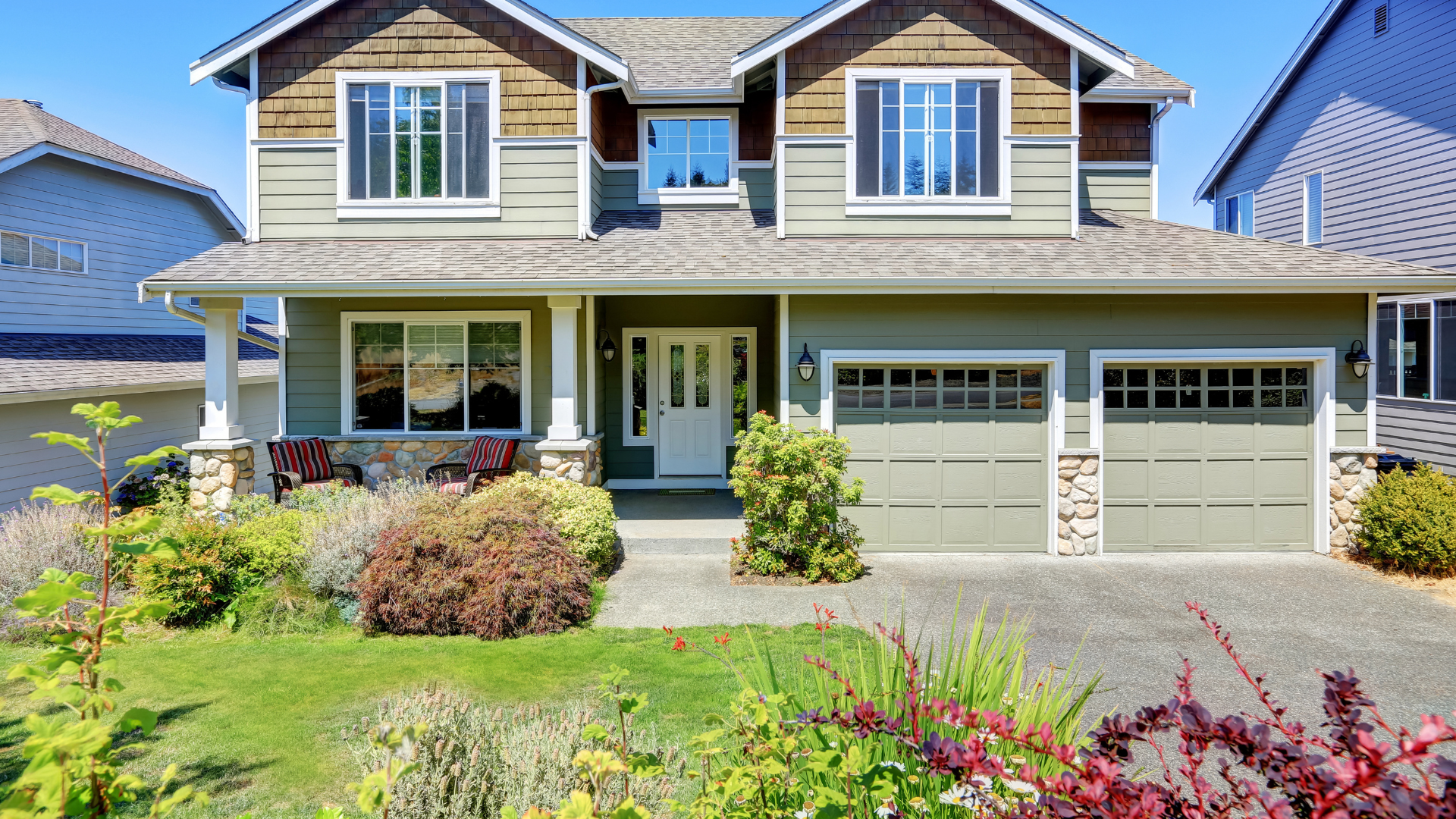 Two-story house with green siding, brown trim, and a concrete driveway. Landscaping in front.