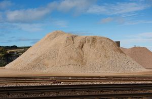 Large pile of light-colored gravel next to railroad tracks against a partly cloudy sky.