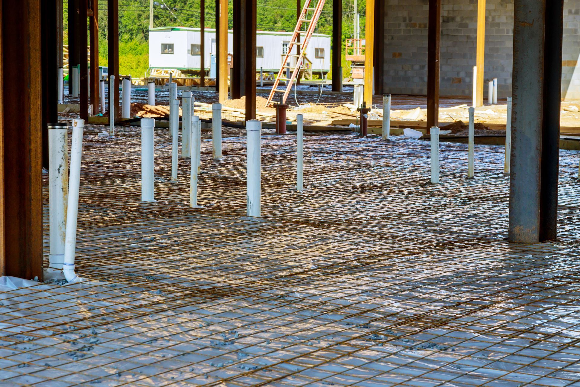 Construction site: concrete floor with PVC pipes and steel beams.