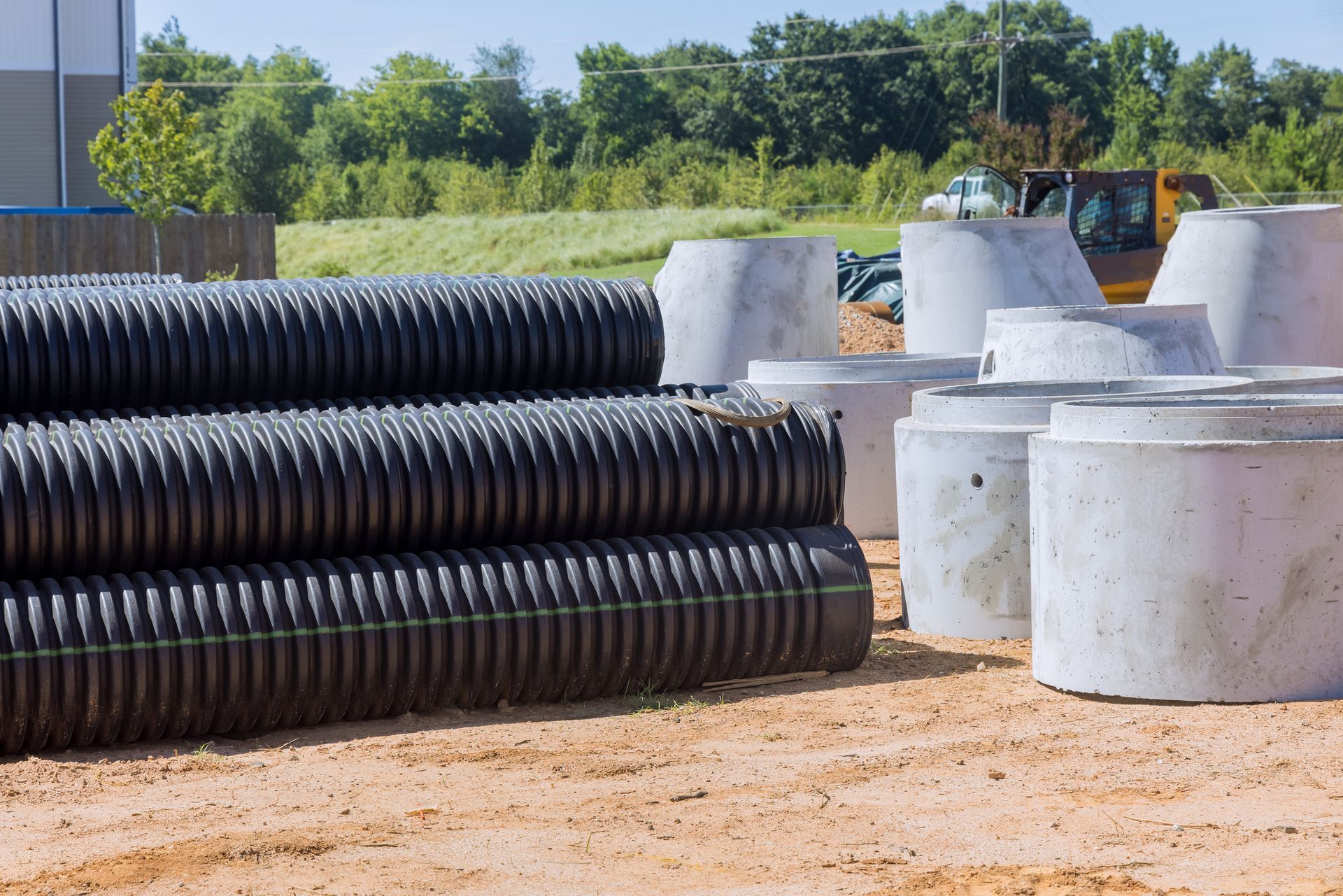Black corrugated pipes stacked next to concrete culvert rings on a construction site.