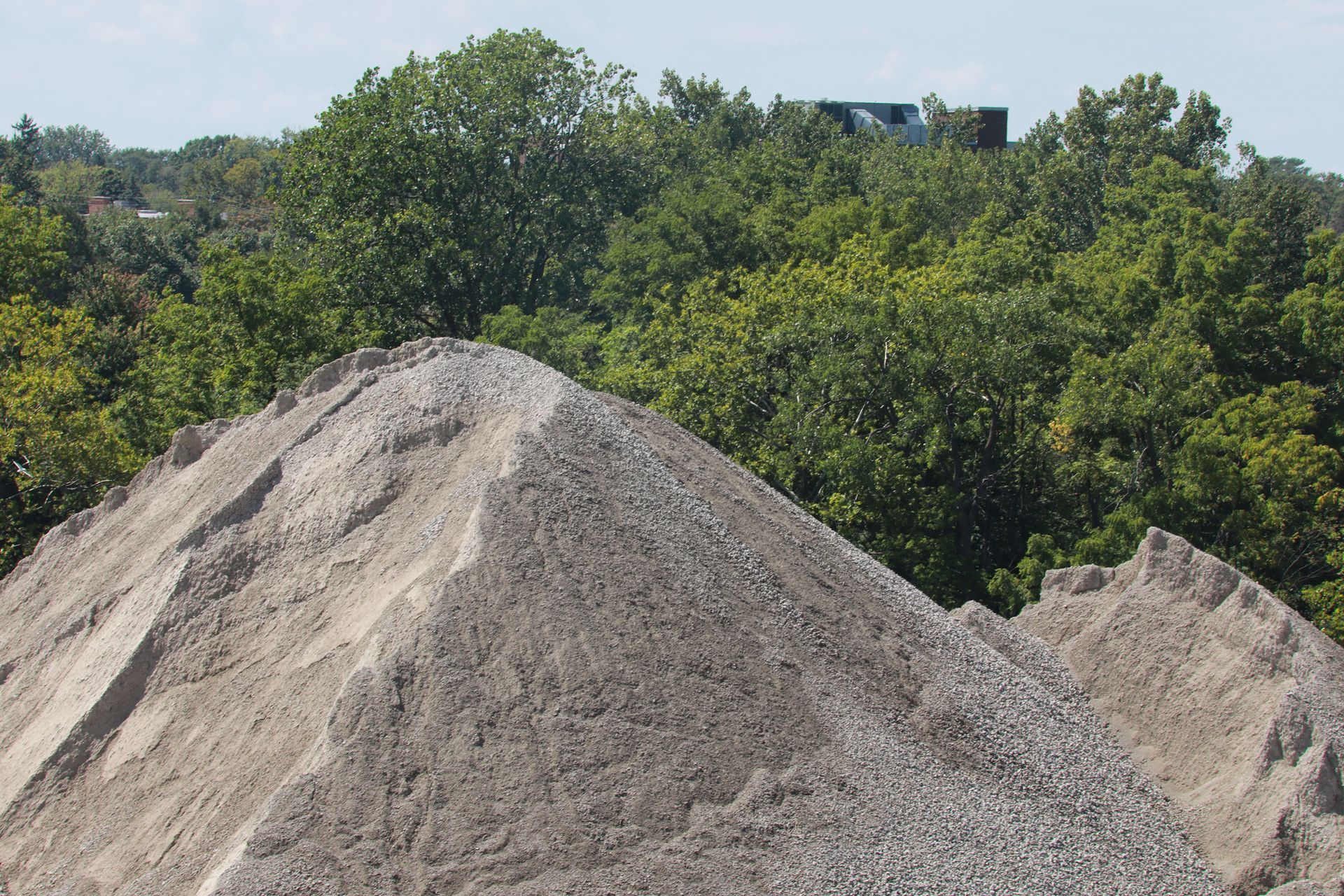 Pile of gravel in foreground, green trees and distant building in background.