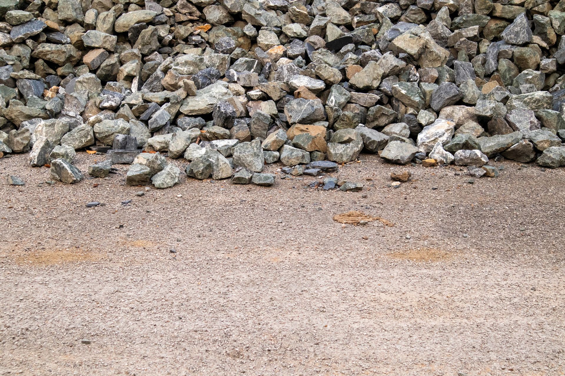 Pile of gray rocks on top of a bed of small, light-brown pebbles.