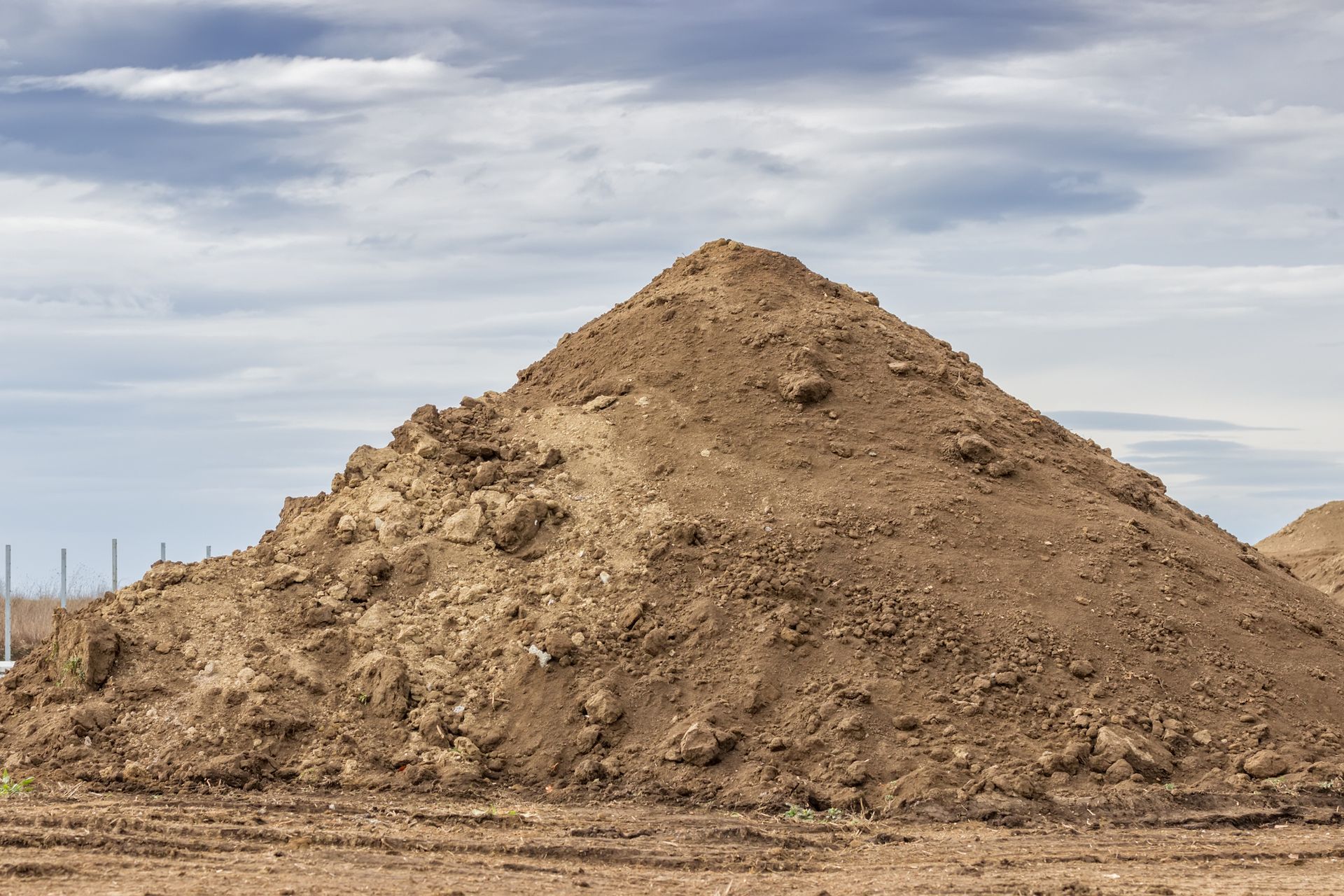 Large pile of brown dirt against a cloudy sky.