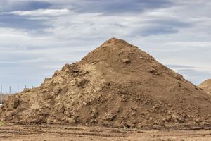 Large pile of brown dirt against a cloudy sky.