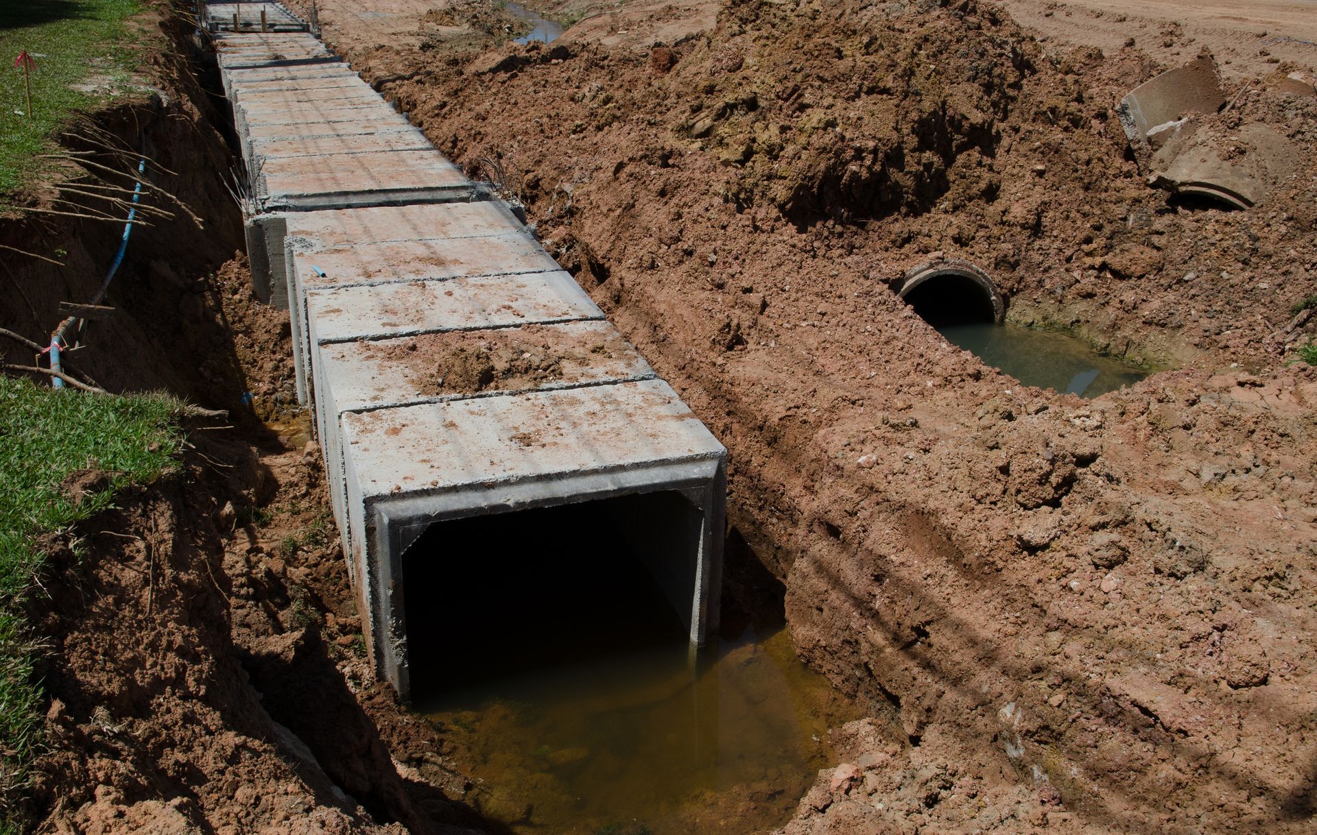 Concrete culvert segments installed in a dirt trench, used for drainage.