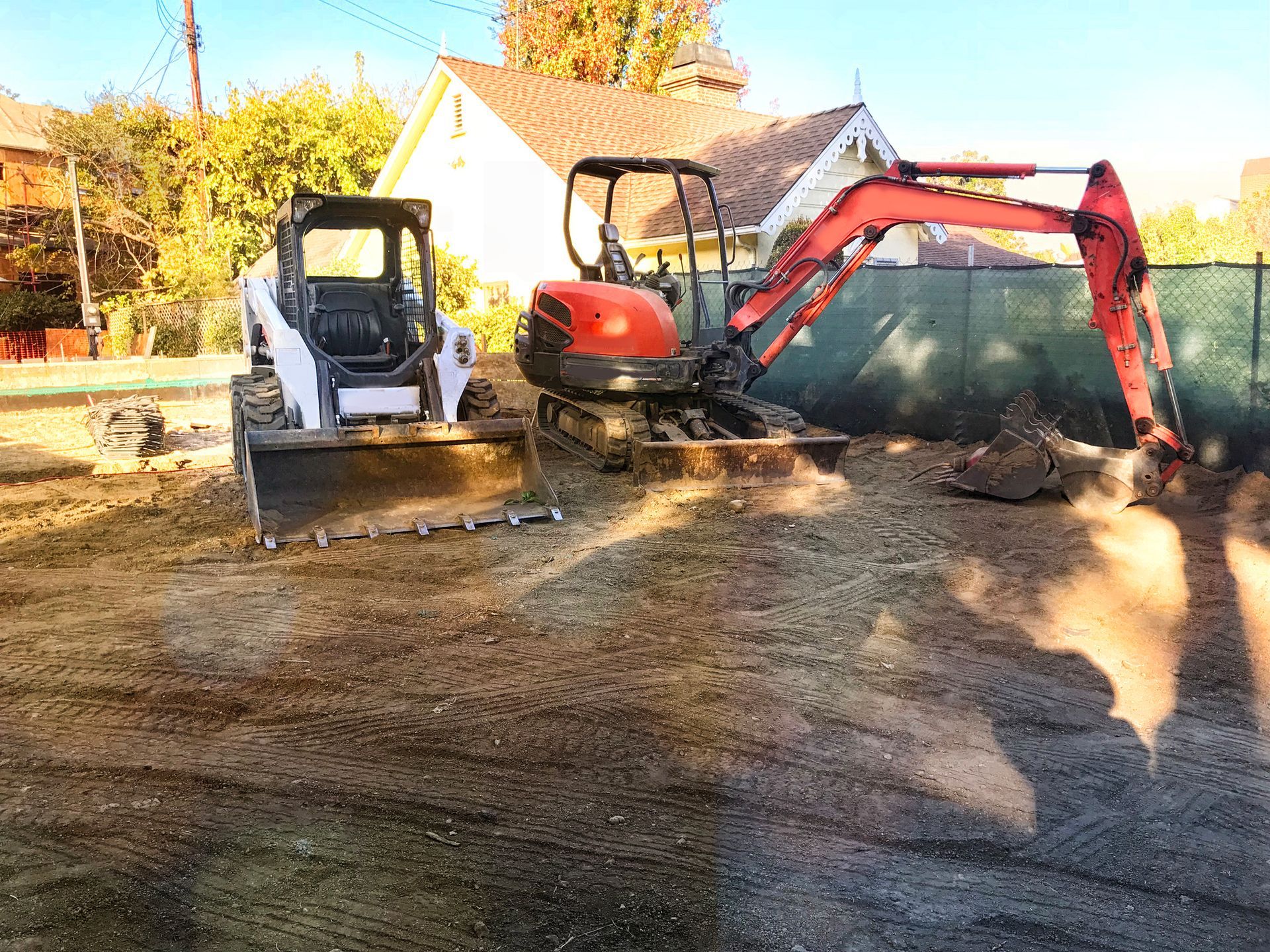 Bobcat and excavator on a dirt lot, preparing a construction site.