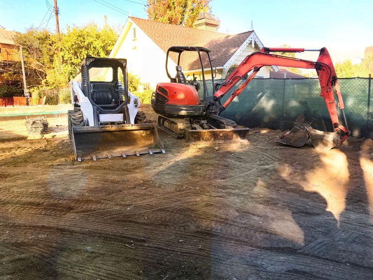 Bobcat and excavator on a dirt lot, preparing a construction site.