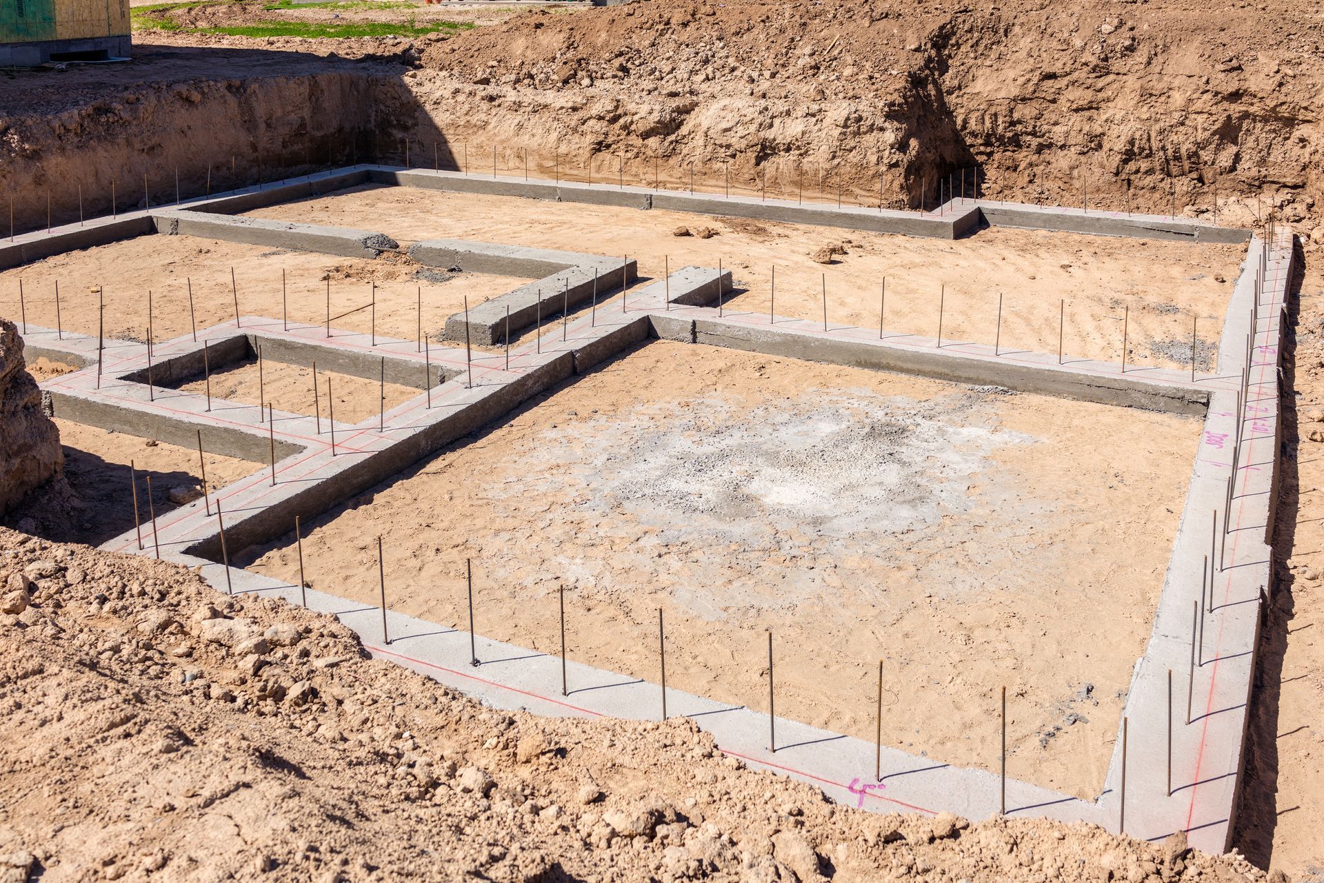 Concrete foundation for a building under construction, set in dirt. Rebar stakes mark wall positions.