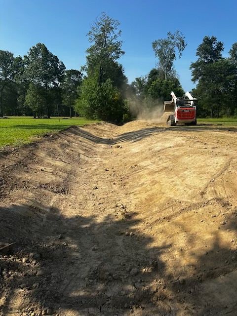 Cleared land with debris and machinery, trees in background, white house on a hill.