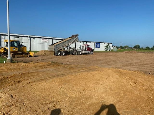 Construction site with leveled ground, cinder block foundations, and lush greenery in the background.