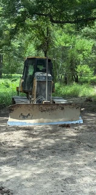 Yellow bulldozer clearing land in front of a forest, under a partly cloudy sky.