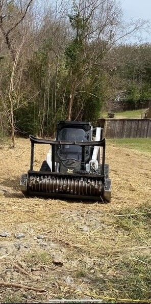 A skid-steer mulcher clearing brush in a snowy field, producing wood chips.
