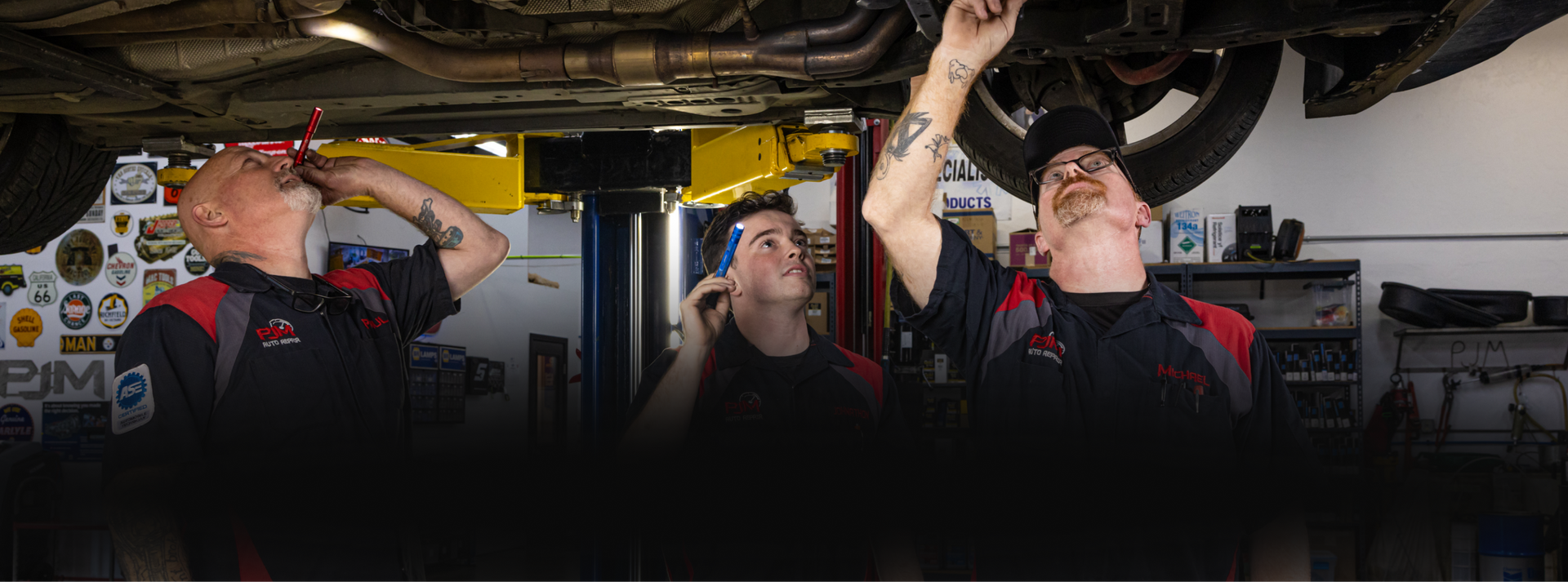Three mechanics inspecting underside of a car in a repair shop. | PJM Auto LLC