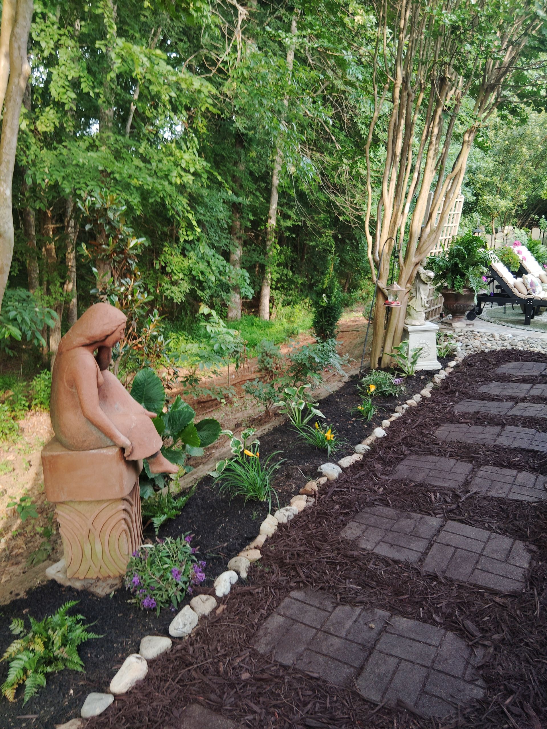 Statue of girl in garden with stone pathway and flower bed.