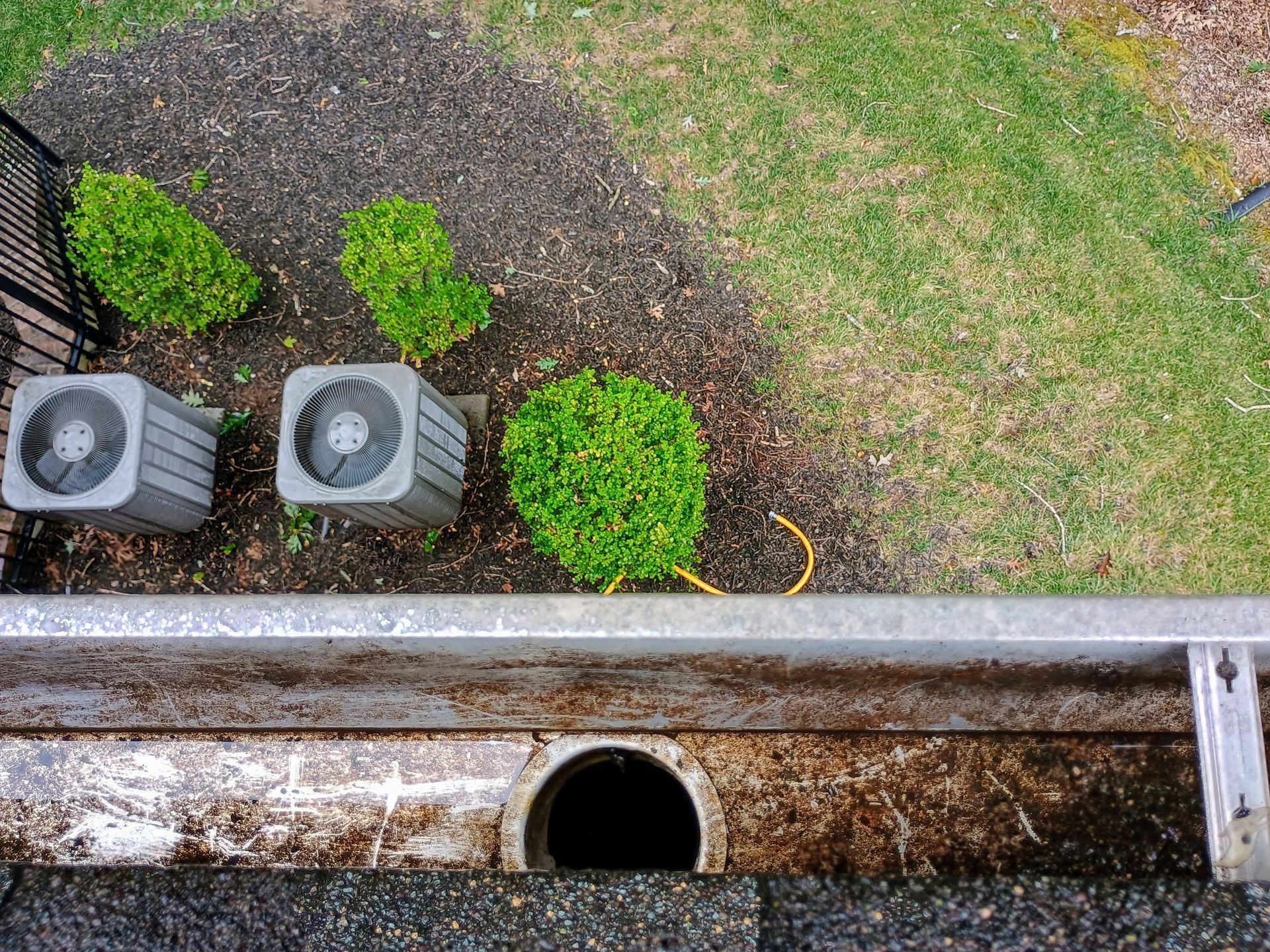 Overhead view of a gutter, drain, and air conditioning units in a yard with landscaping and grass.