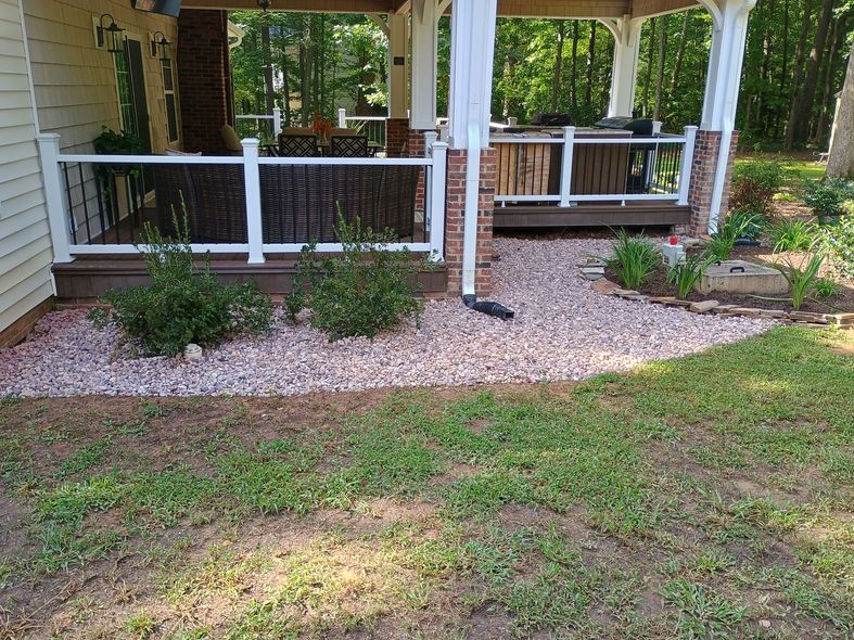 A house patio with pink gravel, green bushes, and a grassy lawn.
