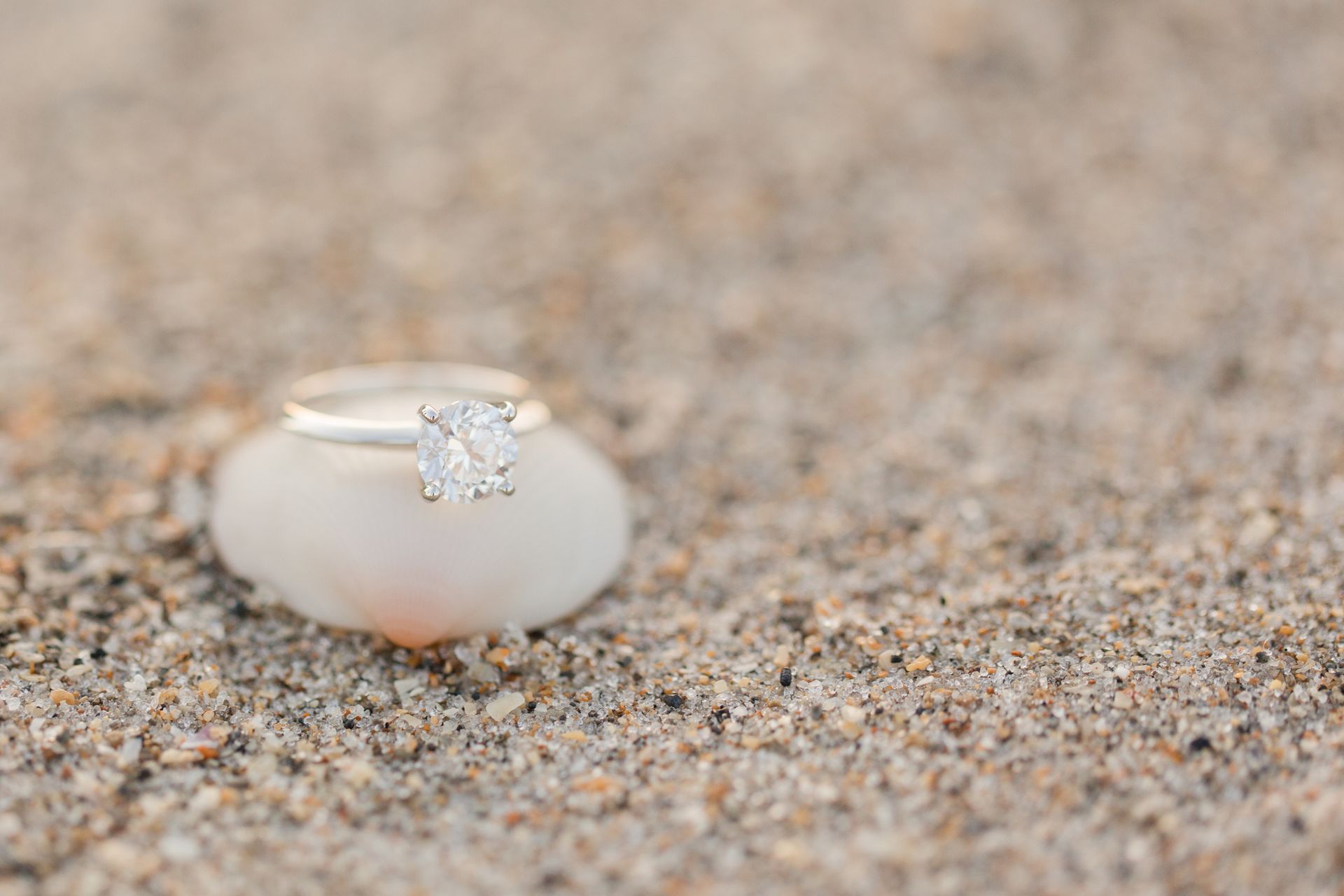 A round diamond ring in white gold on a sandy beach.