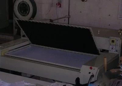 Un'unità di esposizione a vuoto per lastre fotografiche, con il coperchio aperto che rivela un tavolo luminoso all'interno, situata in un'officina industriale.