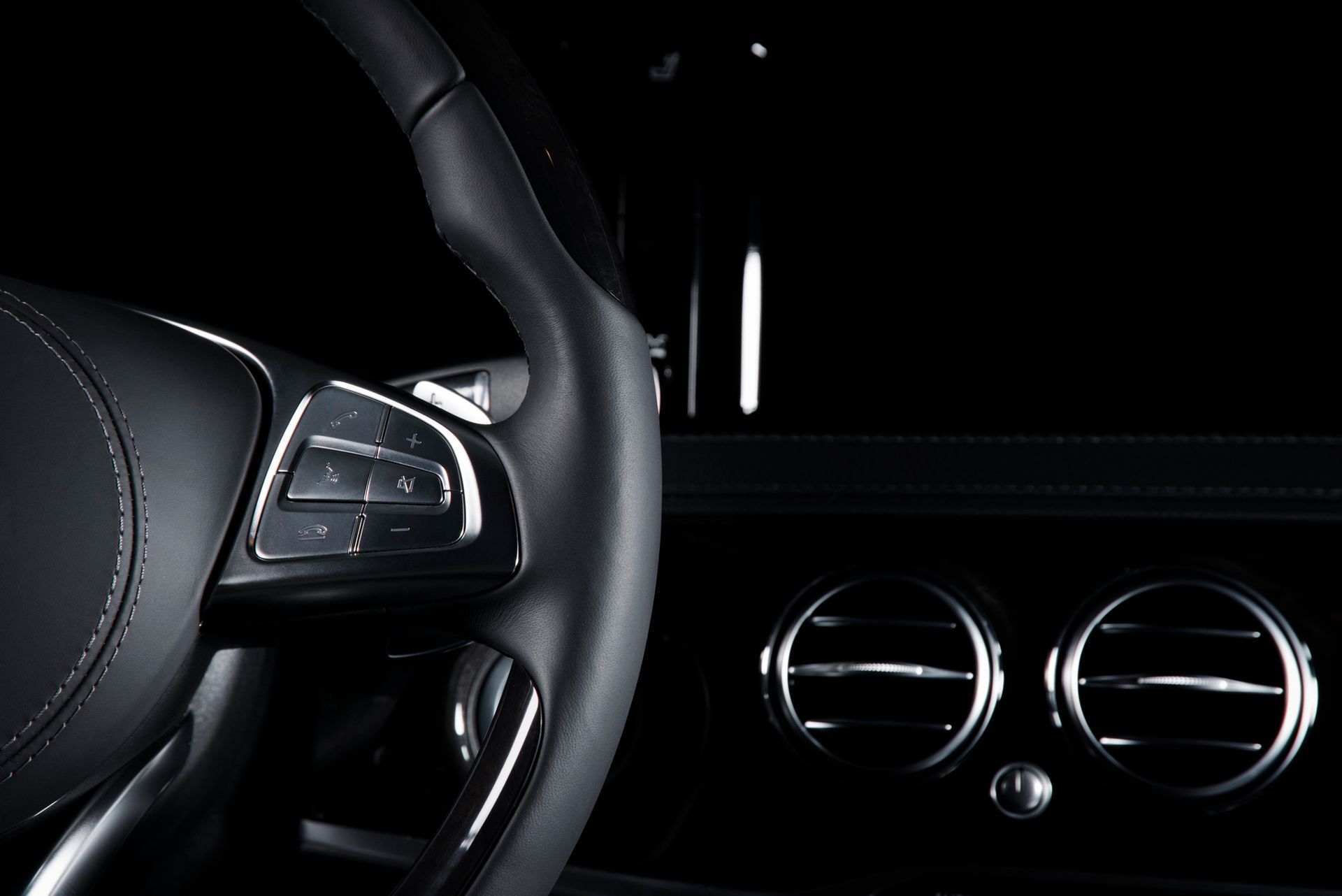 Un primo piano degli interni di un'auto di lusso nera, che mostra il volante e le bocchette dell'aria cromate.