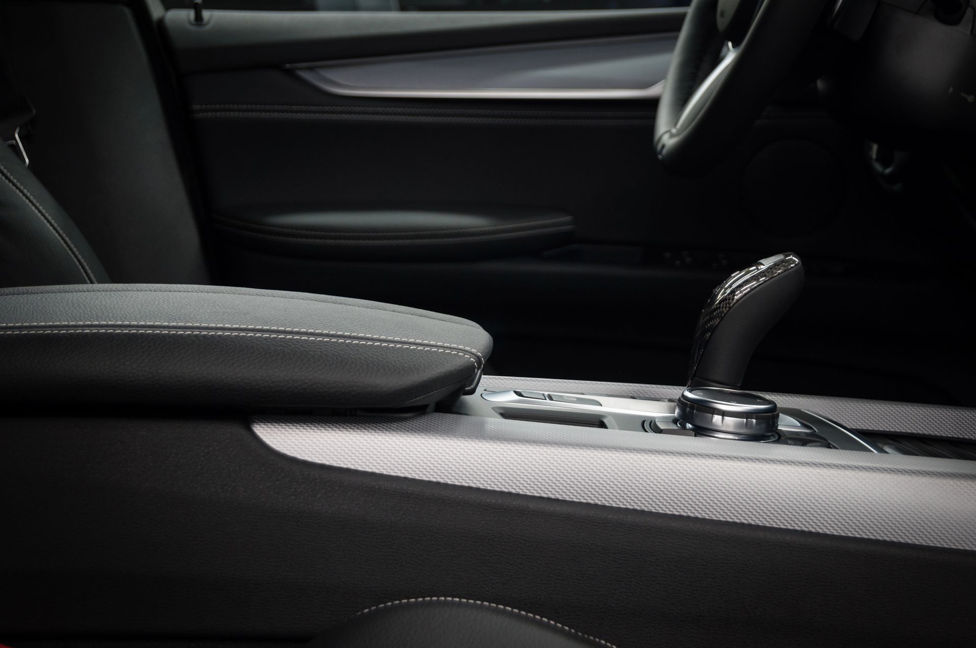 Primo piano degli interni di un'auto moderna che mostra la console centrale in pelle scura, la leva del cambio e i dettagli delle finiture metalliche.